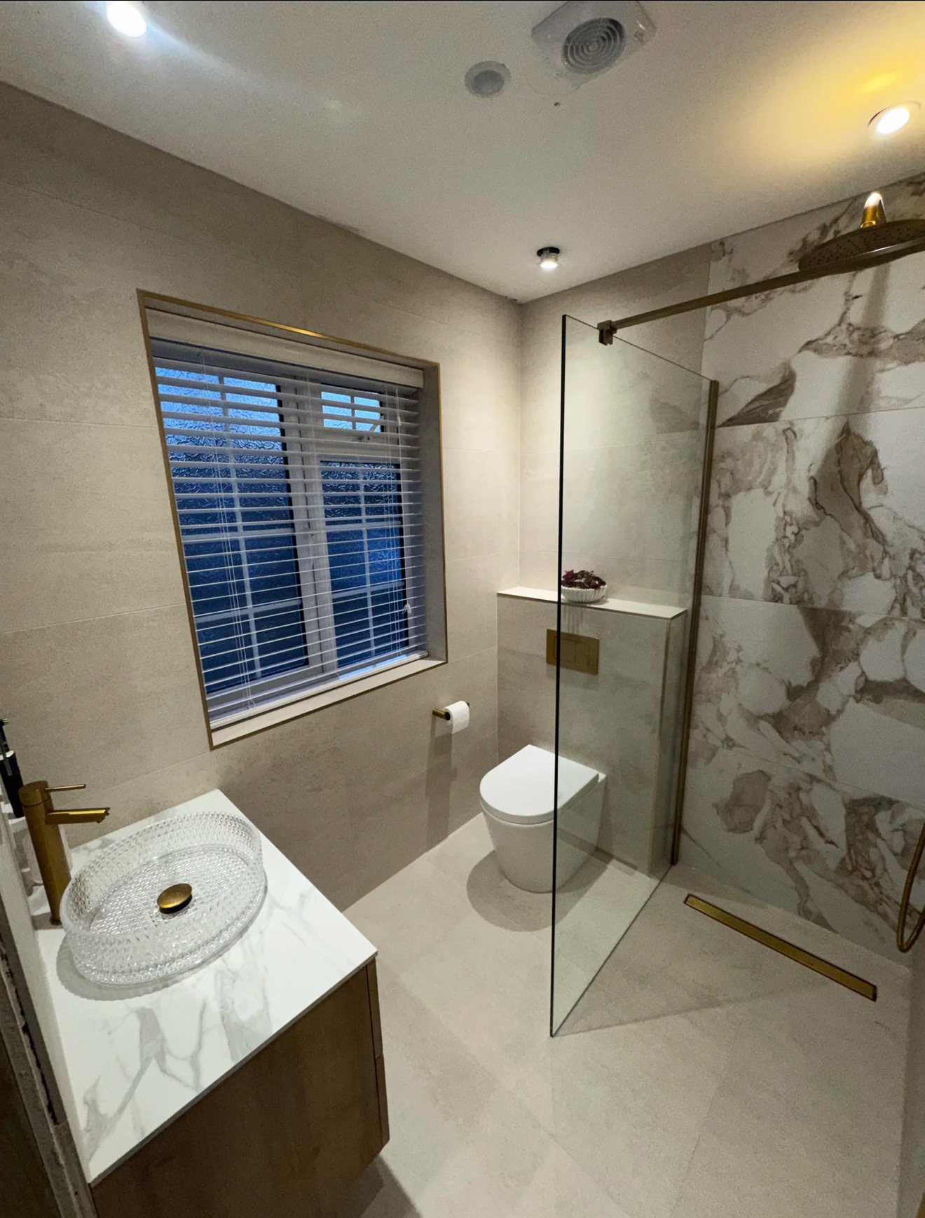 Elegant marble bathroom with clear glass walk-in shower, vessel basin, brass tap and window shutters — installed by Farnham Bathroom Fitters in Farnham, Surrey